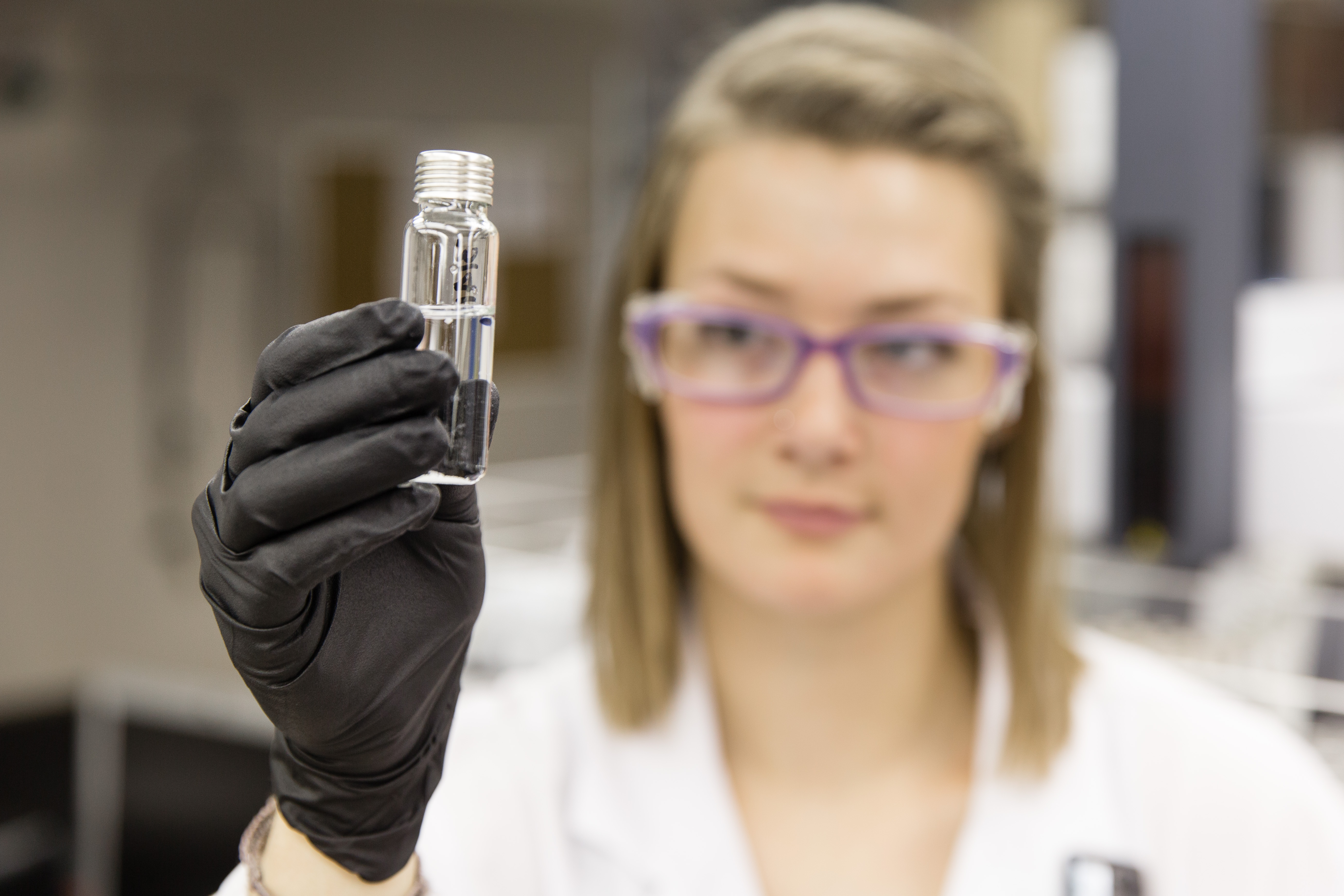 female lab technician looks at vial