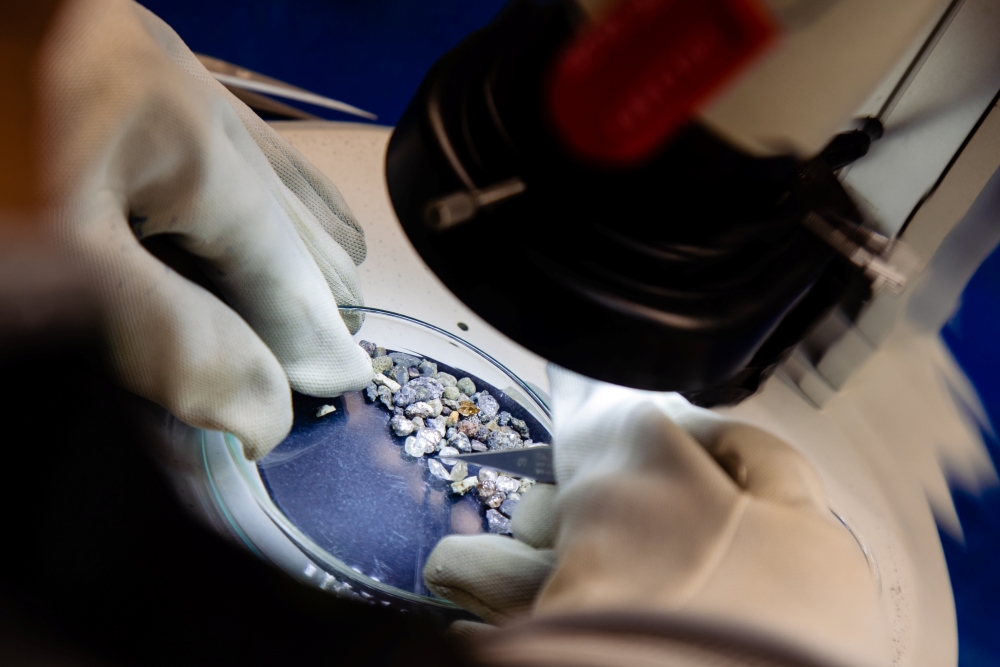 lab technician sorts diamonds in a glass dish under microscope