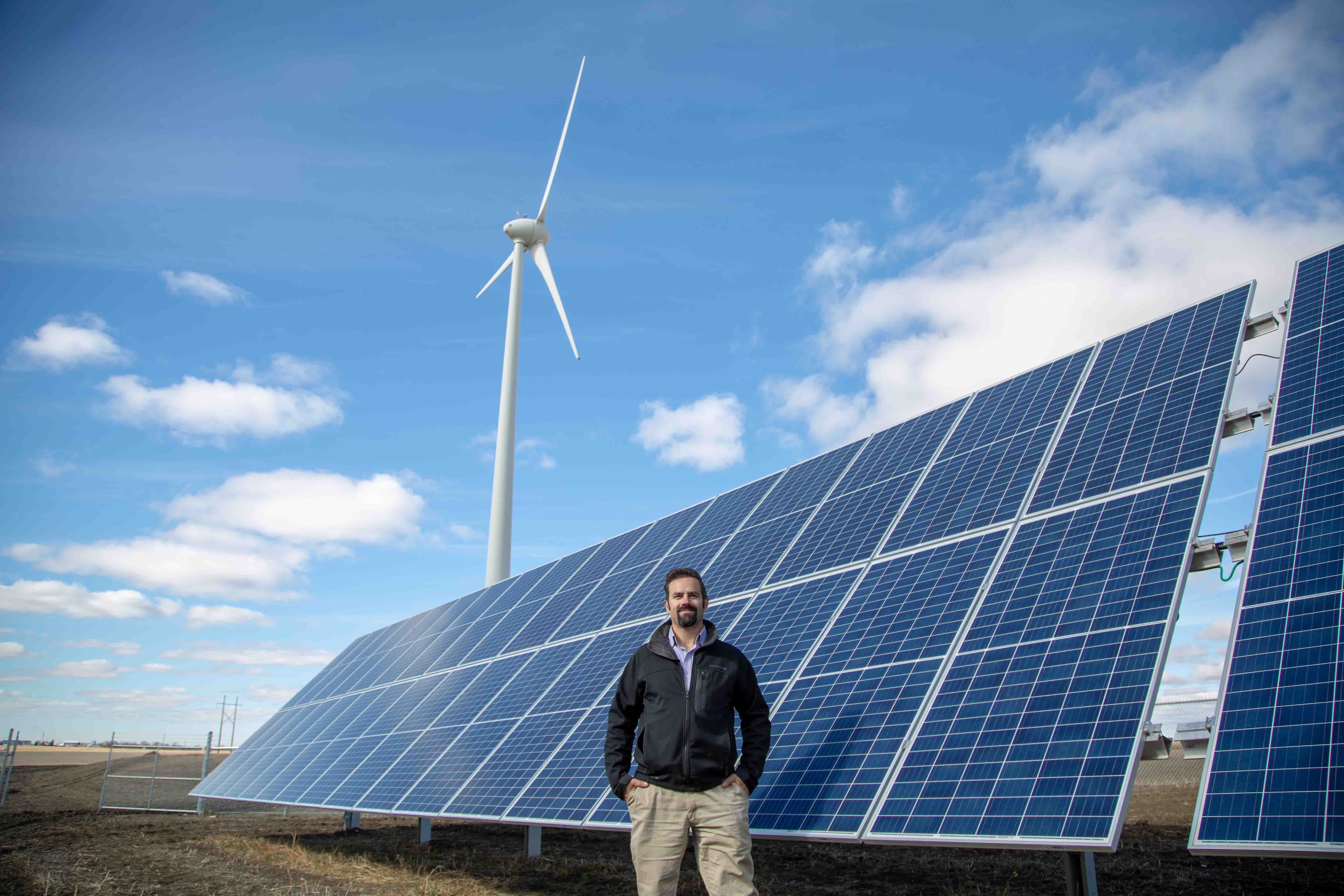 src employee standing in front of wind turbine and solar panels