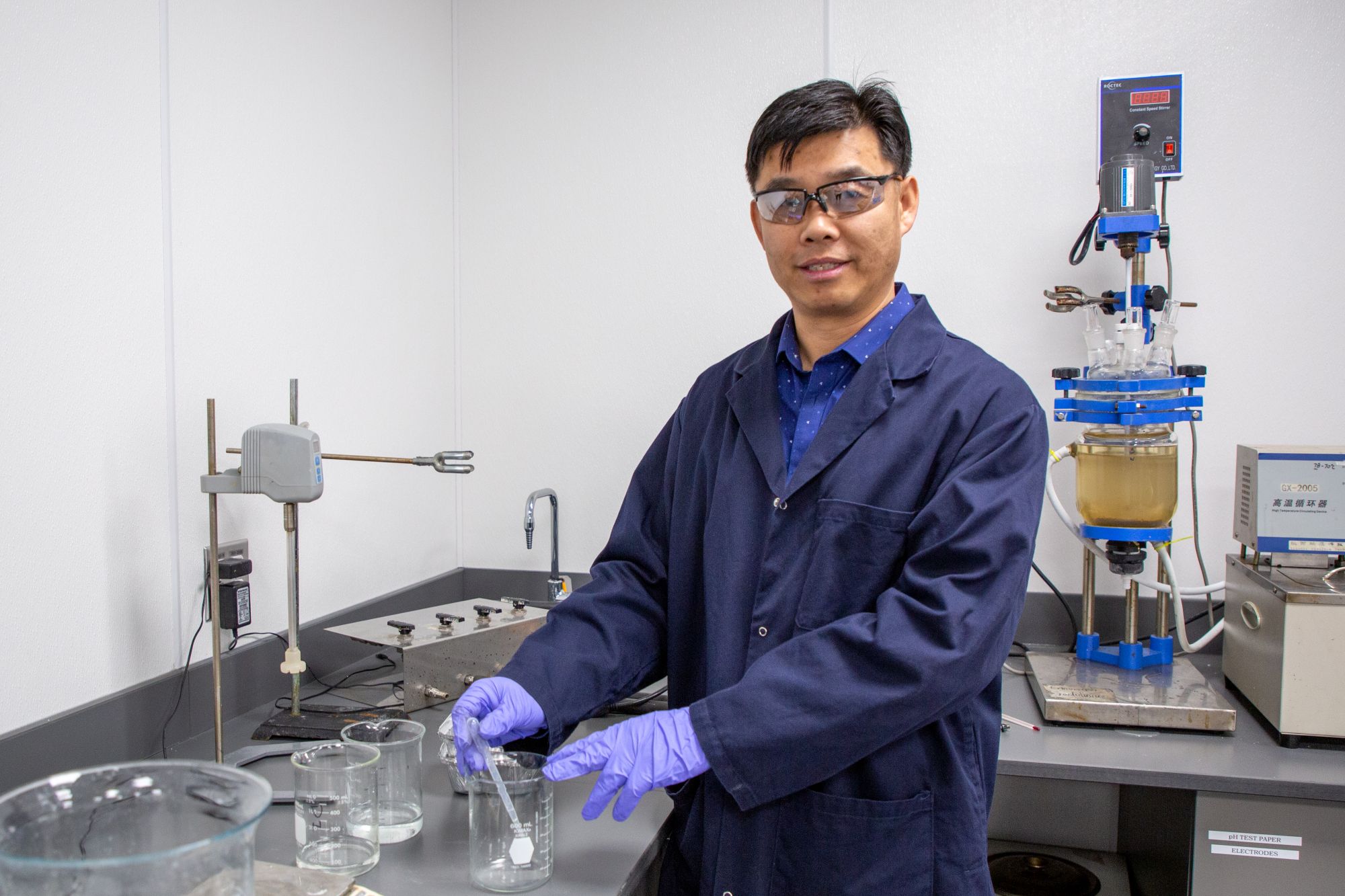 man in blue lab coat stands in lab holding beaker