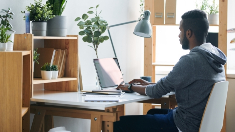 man working from home at computer desk with plants and lamp