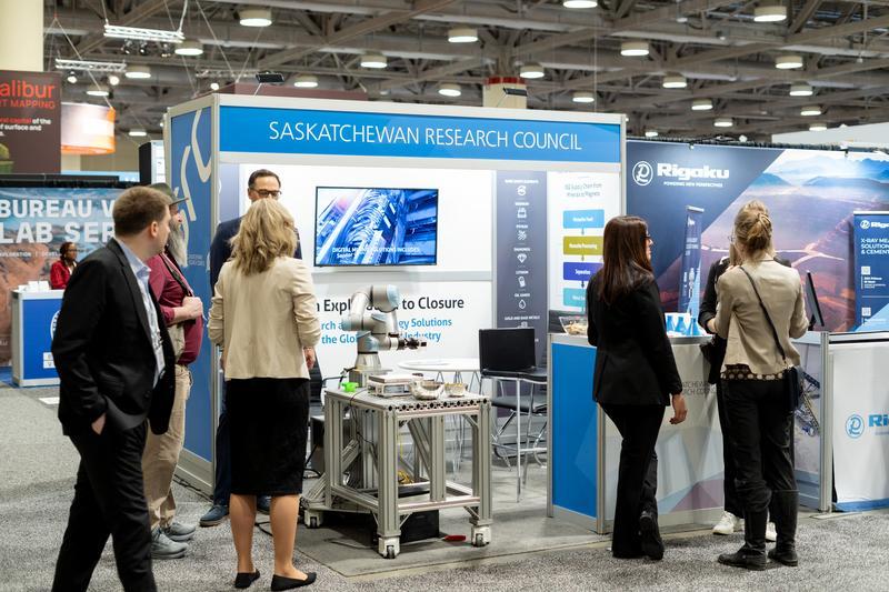 src employees and conference attendees gathered around src's tradeshow booth featuring a "robot arm"