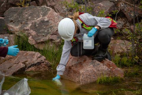 female technician collecting water into bottle from lake