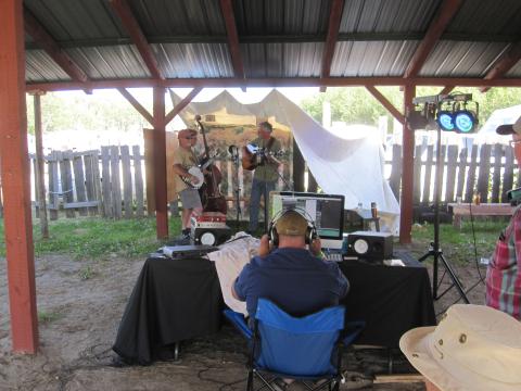 Outdoor recording studio with audio engineer in front and band in background under a tent.