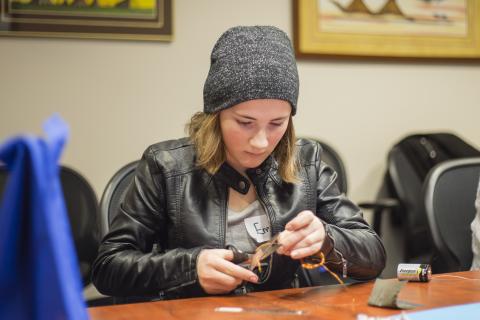 Female high school student creates electricity using a battery and wire