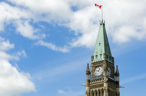 Parliament building with Canada flag with blue sky and clouds in background