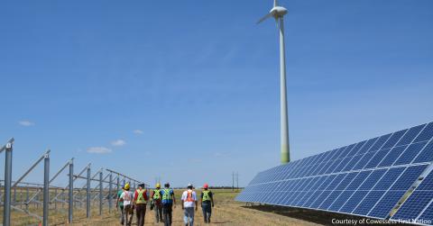 field workers walking towards src cowessess wind turbine with solar panels