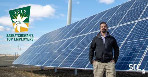 src employee stands in front of solar panel with sask top employer logo