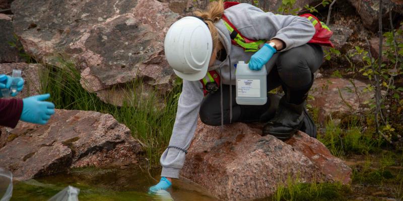 female technician collecting water into bottle from lake