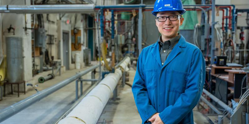 Dexu K stands in front of industrial setting at SRC's Pipe Flow Facility