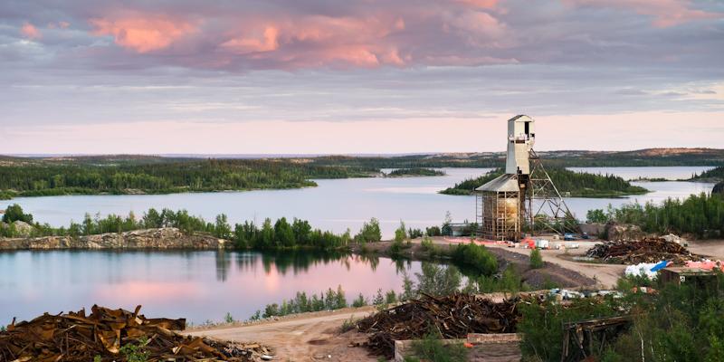 debris piles and headframe in remote lake area against sunset