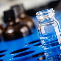 small vial with clear liquid and darker bottles in blue rack at src lab