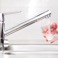 hand holding glass under running faucet to test for src lead in drinking water