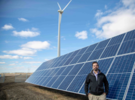 src employee stands in front of cowessess solar panels and wind turbine